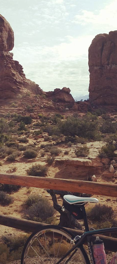 Tall narrow photo of the American West with the back of a bicycle resting against a rustic wood fence